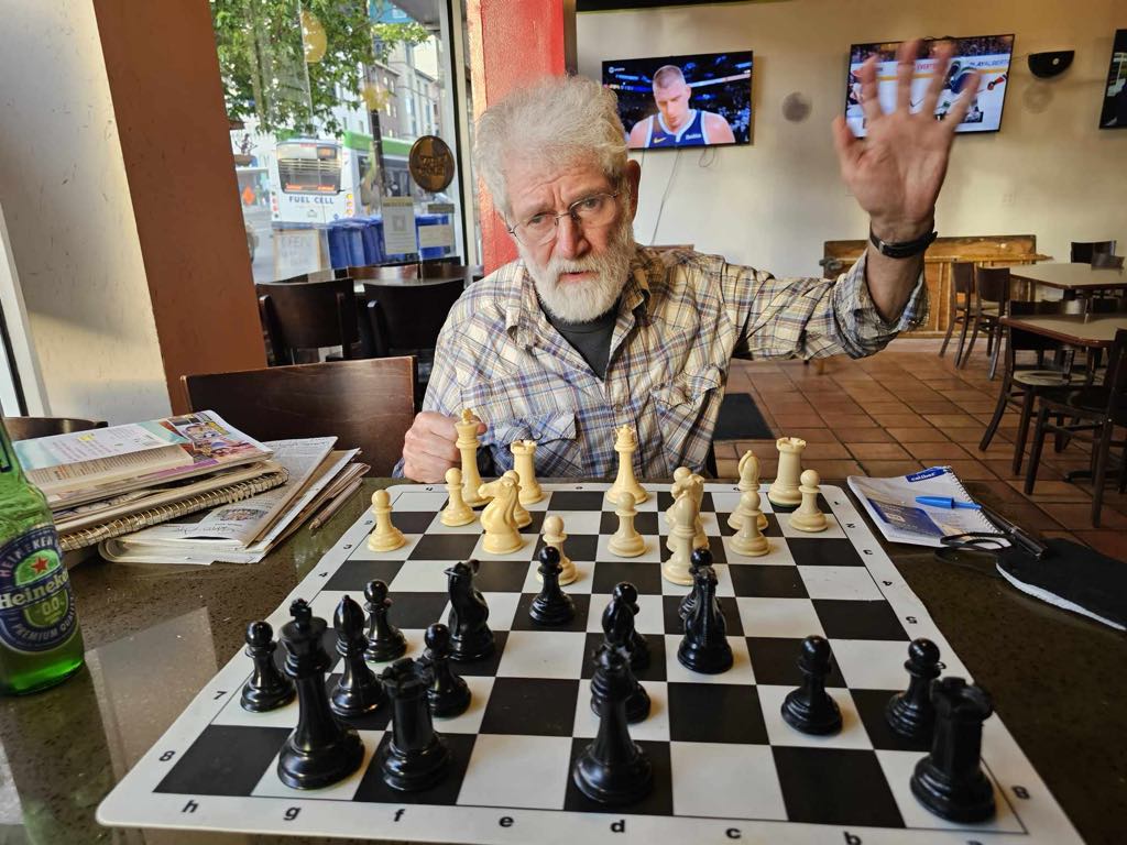 Eric at a chessboard at Bobby G's waving to the camera